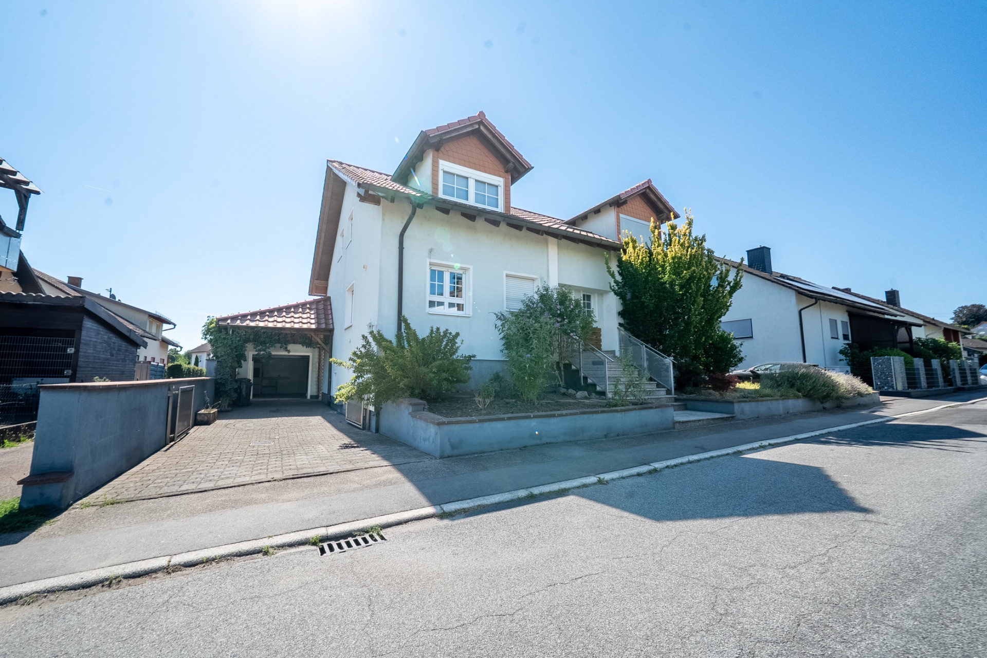 Zweistöckiges Wohnhaus mit Garten und Auffahrt, fotografiert bei sonnigem Wetter von der Straße aus.