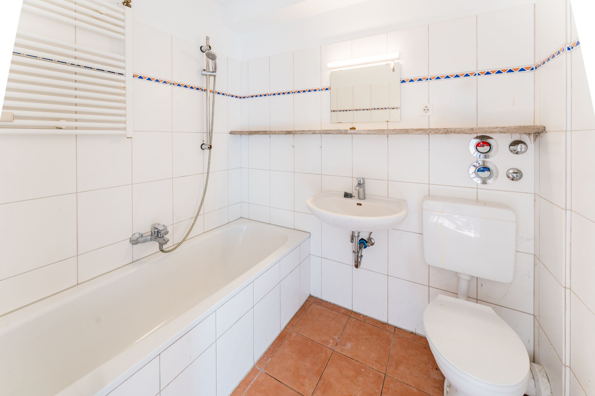 Kleines Badezimmer mit Badewanne, Waschbecken, Toilette und weißer Fliesenwand.