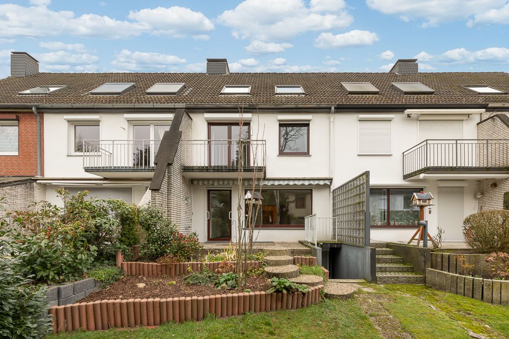 Rückseite eines Reihenhauses mit Balkon, Terrasse, Garten und Kellerabgang.