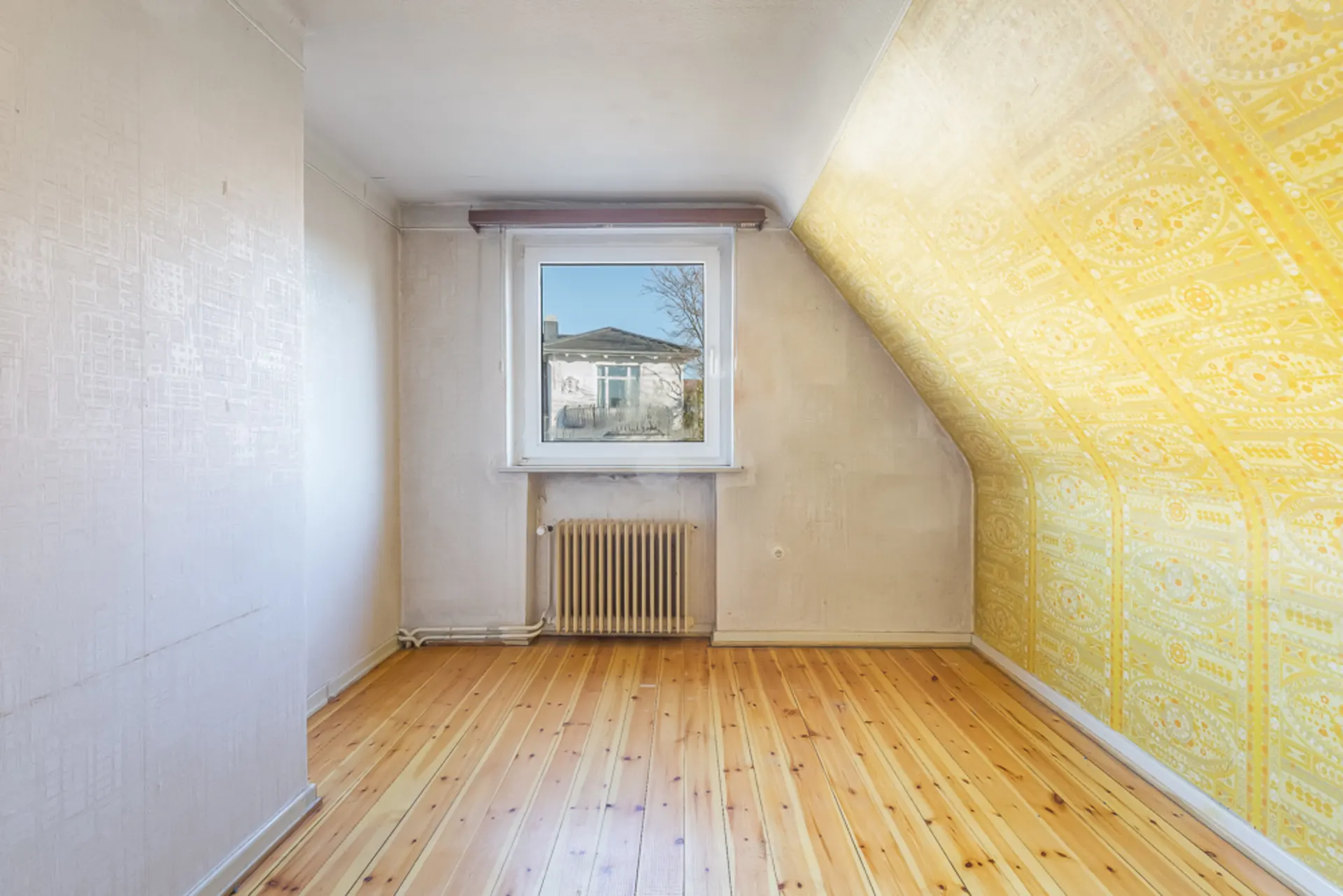 Leerer Raum mit Holzfußboden, einem Fenster und einer gelb gemusterten Schräge.