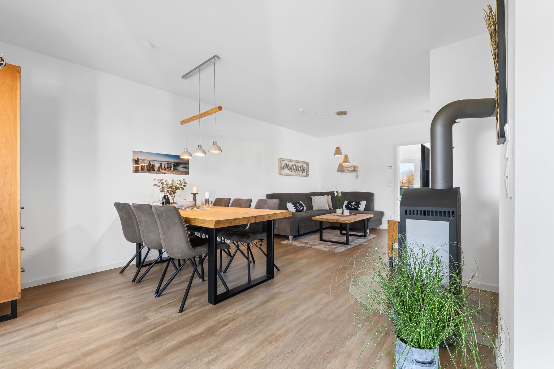 Modernes Wohnzimmer mit Esstisch, grauem Sofa, Holzofen und hellen Holzböden.