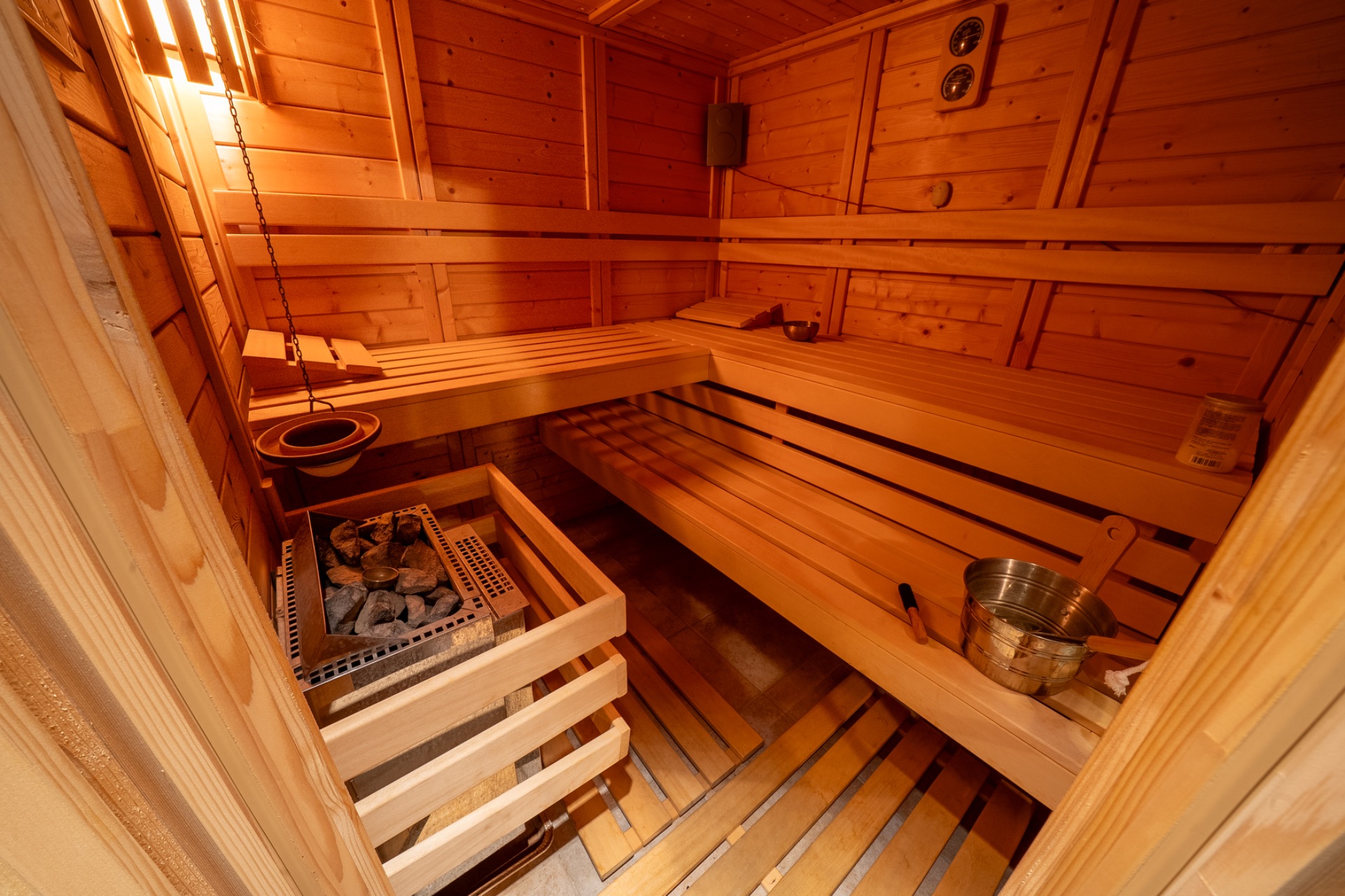 Holzsauna mit Bänken, Saunaofen und Wassereimer.