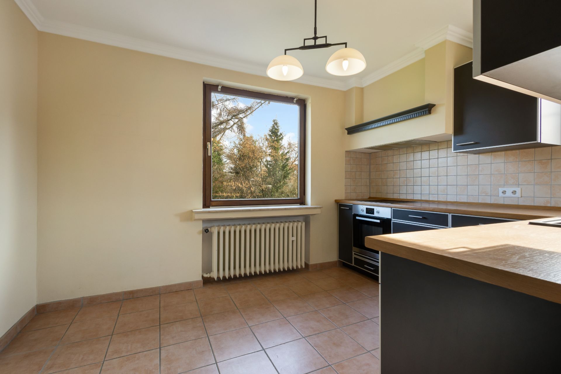 Helle Küche mit großem Fenster, dunklen Schränken, Herd und Fliesenboden.