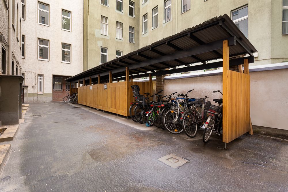 Überdachter Fahrradabstellplatz mit mehreren Fahrrädern im Innenhof eines Wohngebäudes.