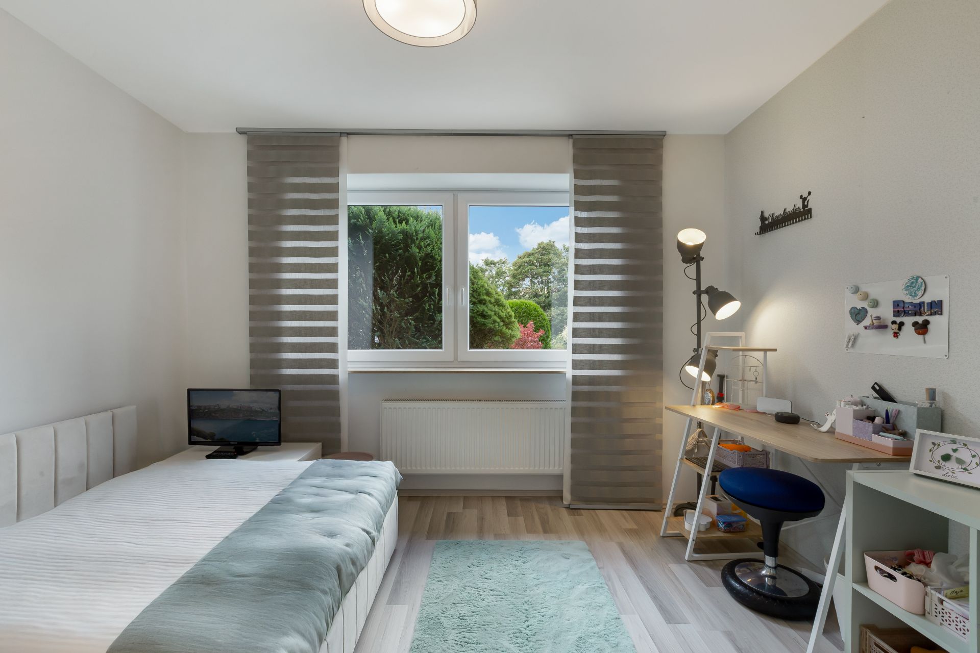 Helles Schlafzimmer mit Einzelbett, Schreibtisch, Stuhl und Fenster mit Blick ins Grüne.