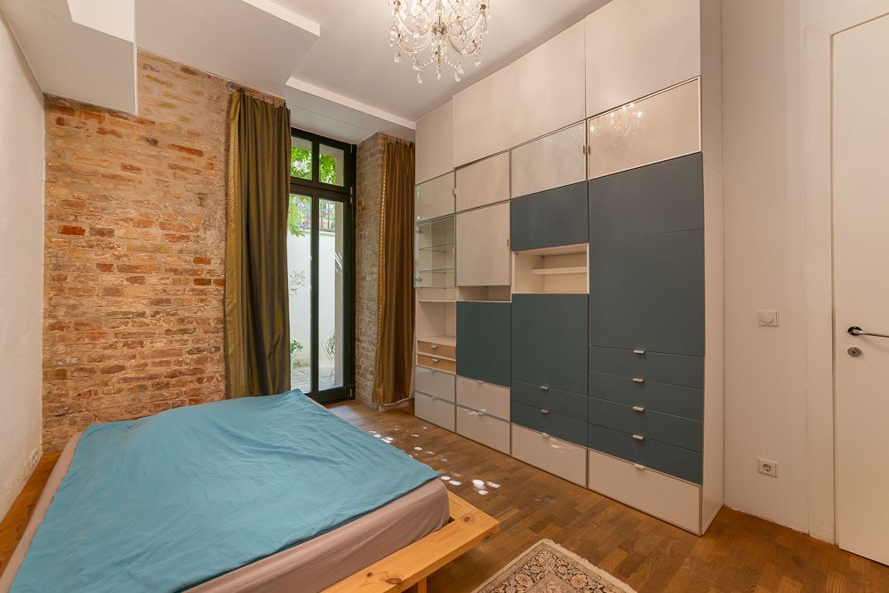 Schlafzimmer mit Holzbett, großer Schrankwand, Parkettboden und Ziegelwand neben Fenster und Vorhängen.