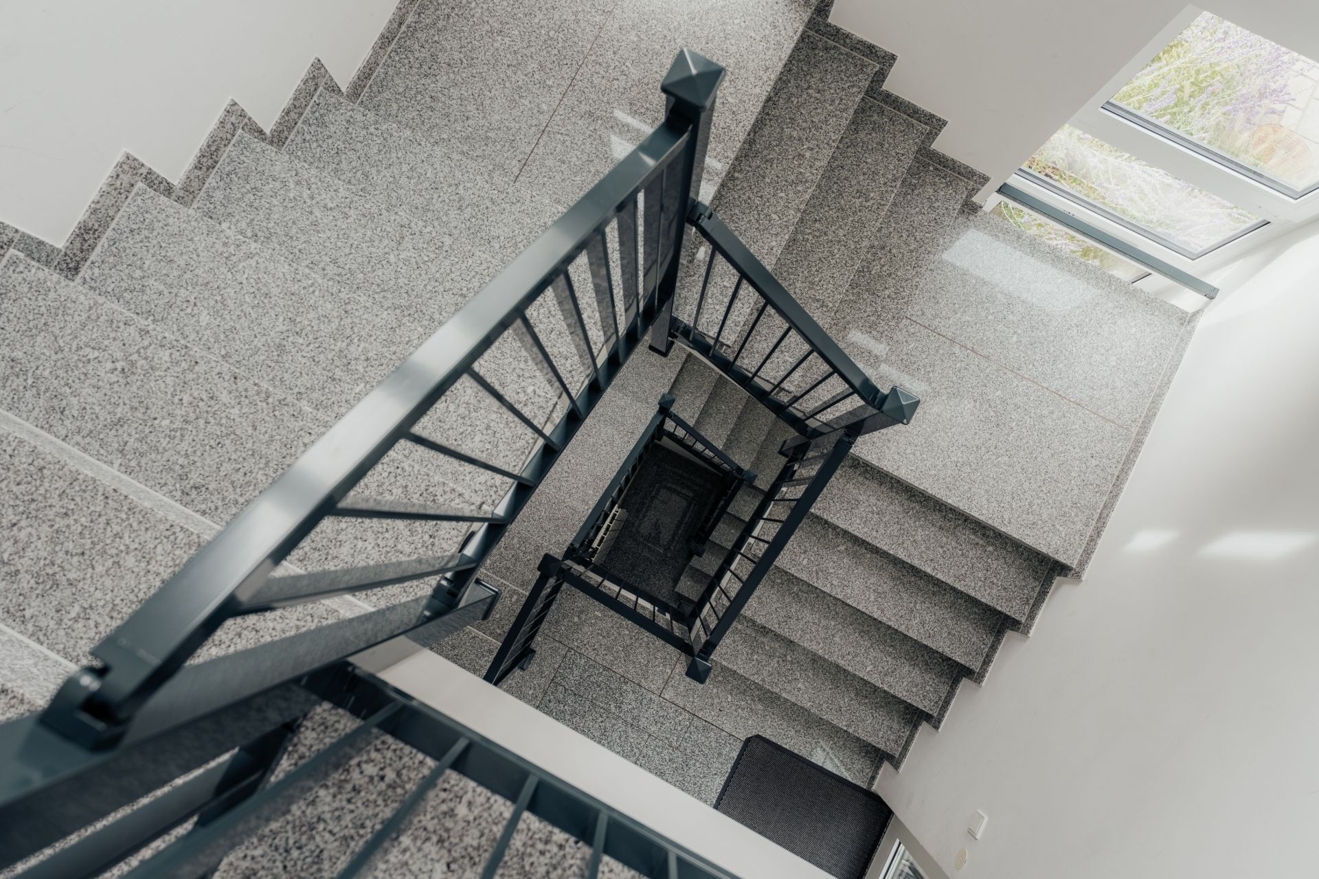 Blick von oben auf ein Treppenhaus mit grauen Stufen und Metallgeländer.