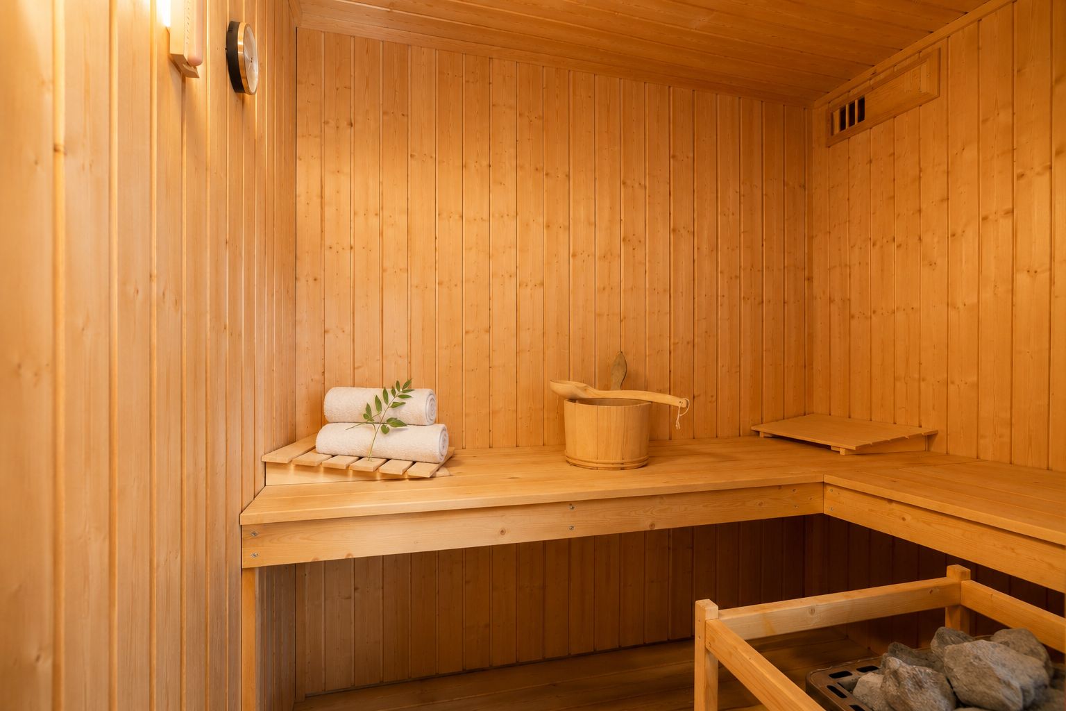 Holzsauna mit Handtüchern, Aufgusseimer und Saunaofen auf der rechten Seite.