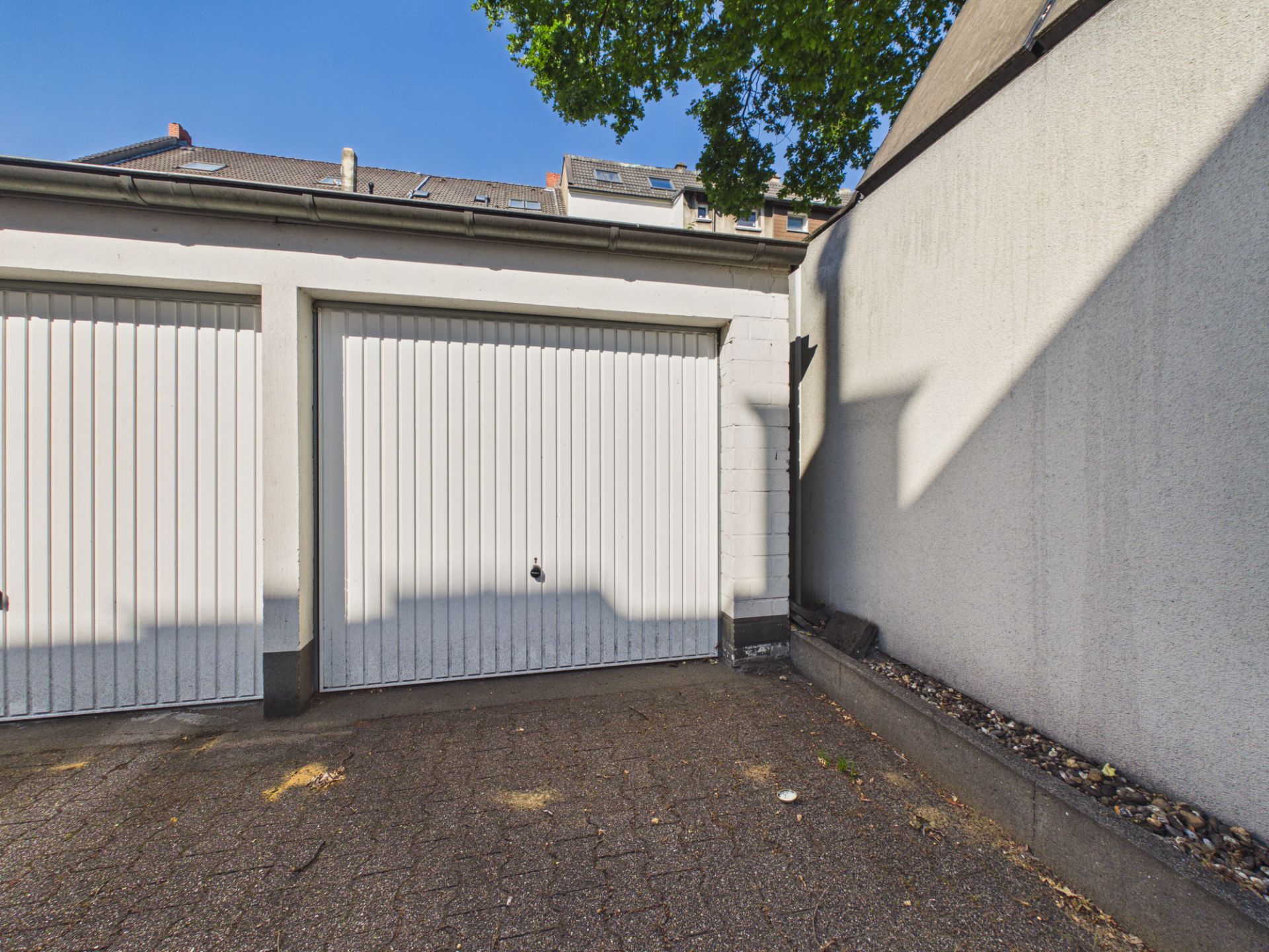 Zwei weiße Garagentore und ein gepflasterter Hof neben einer hohen Mauer.