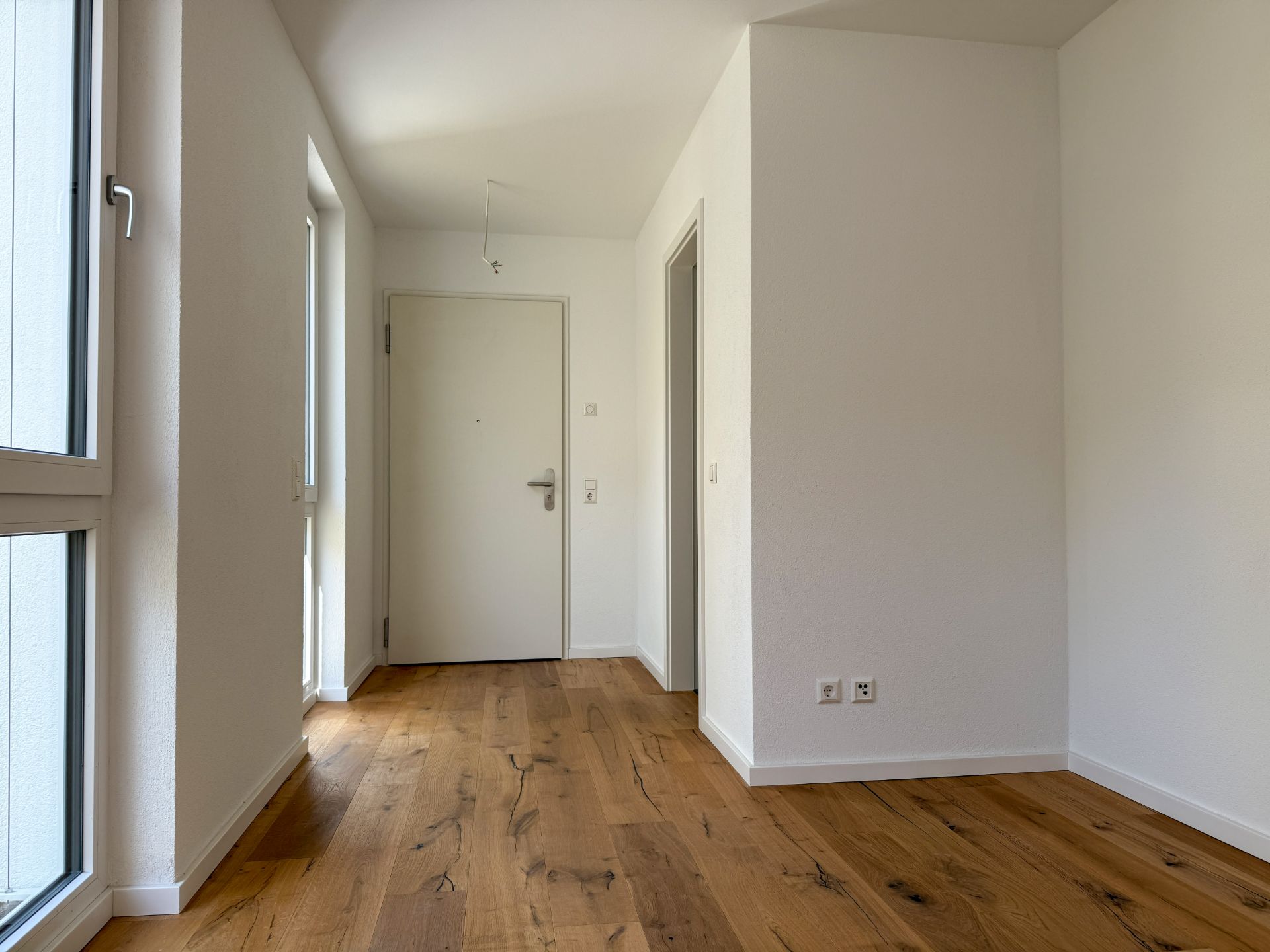 Heller Flur mit Holzboden, weißen Wänden und mehreren Türen in einer Wohnung.