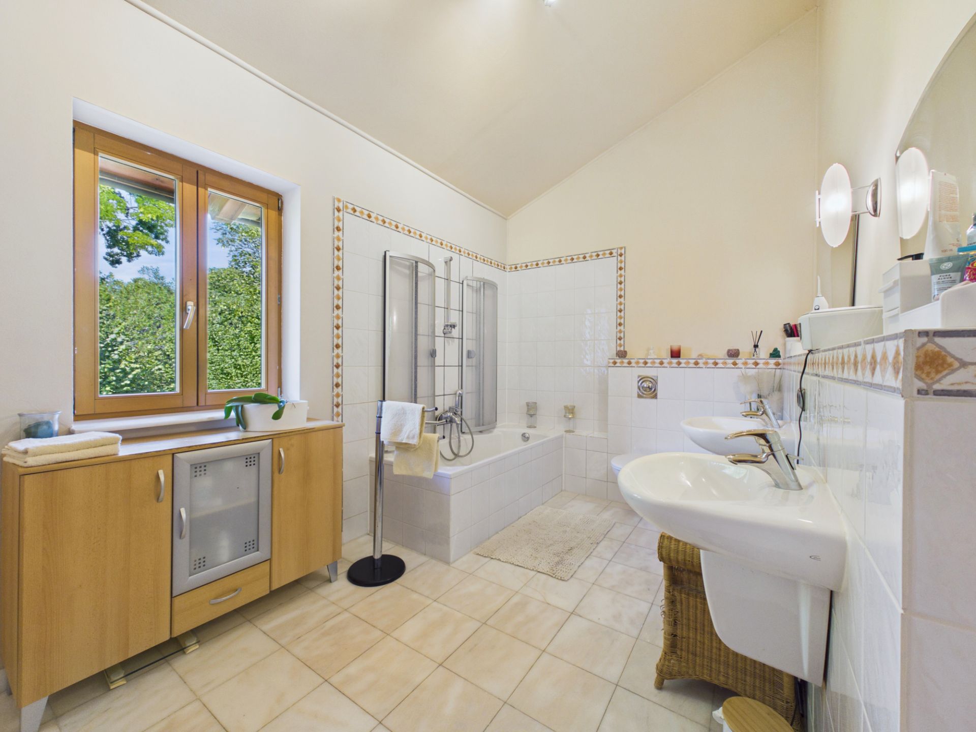 Helles Badezimmer mit Badewanne, Waschbecken, Holzschrank und Fenster.