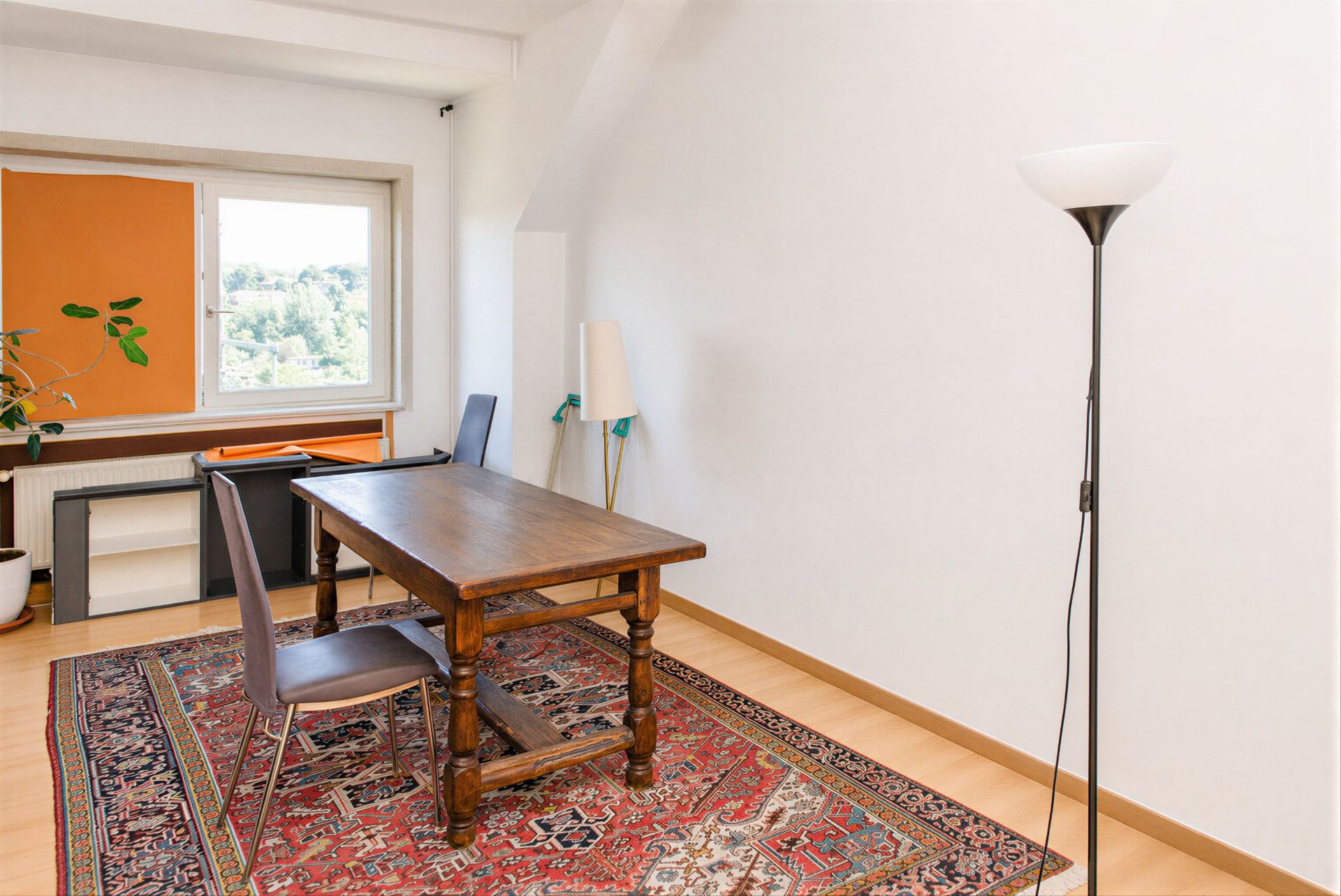 Helles Zimmer mit Holztisch, zwei Stühlen, Stehlampe und Teppich auf Holzfußboden.