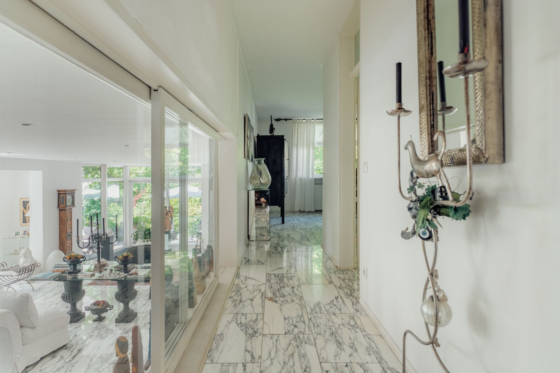 Heller Flur mit Marmorboden, Spiegel und Blick in ein Wohnzimmer mit großen Fenstern.