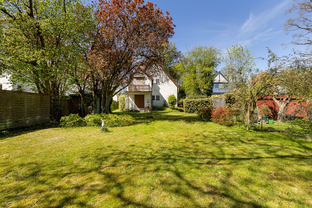 Großer Garten mit Rasen, Bäumen und Blick auf ein weißes Wohnhaus im Hintergrund.