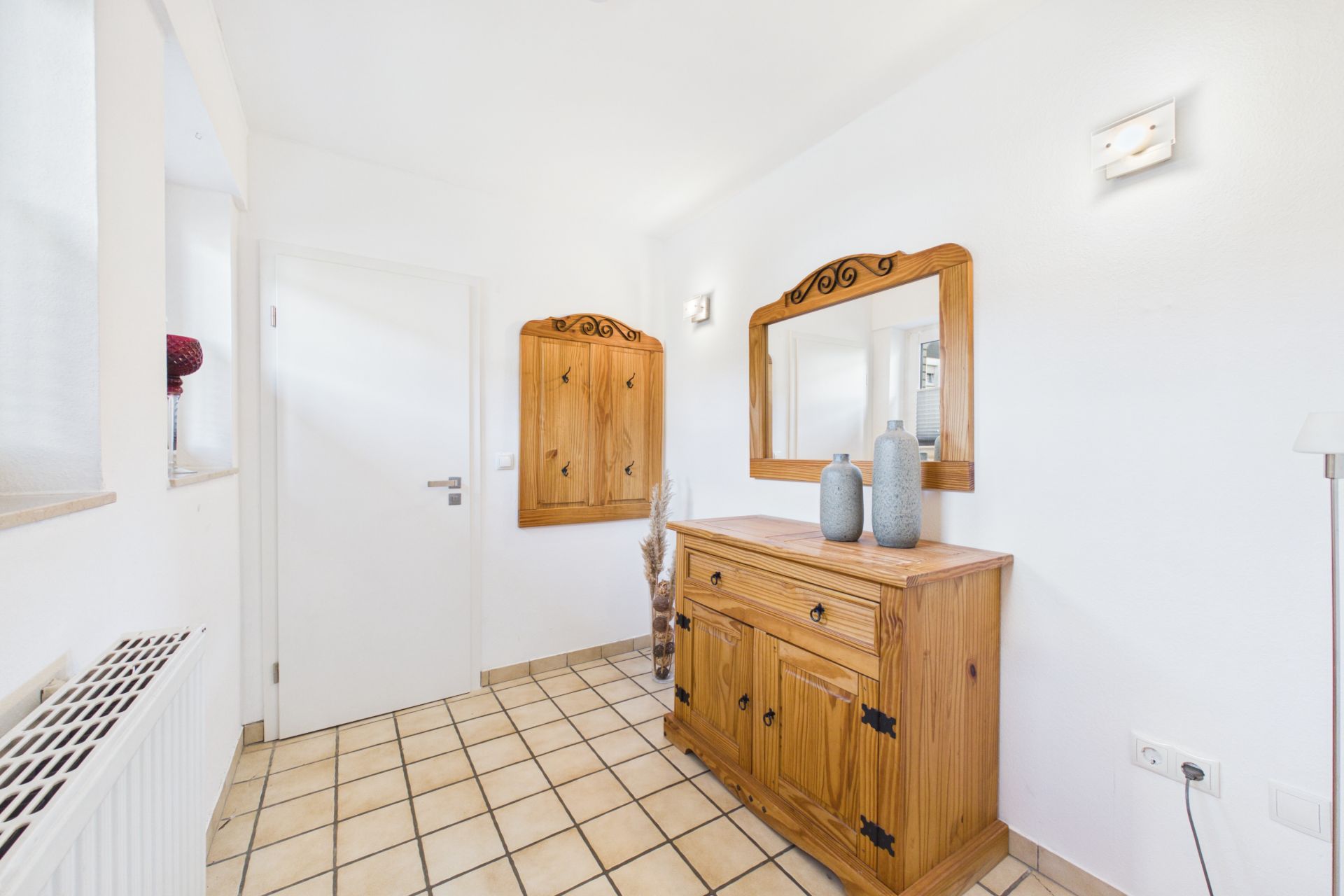 Heller Flur mit Holzkommode, Spiegel und Vasen auf gefliestem Boden.