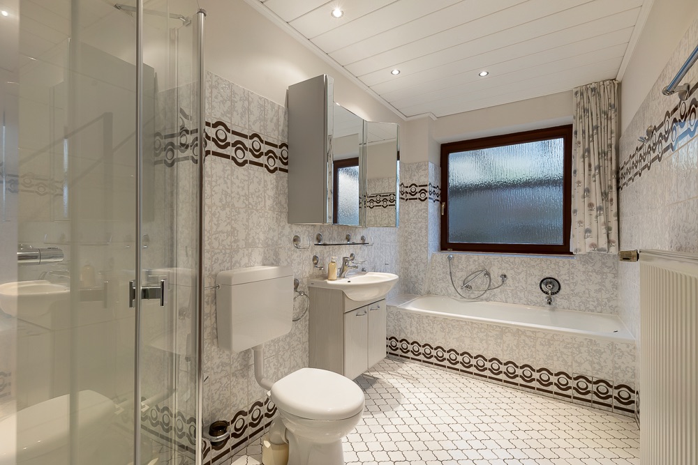 Helles Badezimmer mit Dusche, Toilette, Waschbecken, Badewanne und großem Fenster.