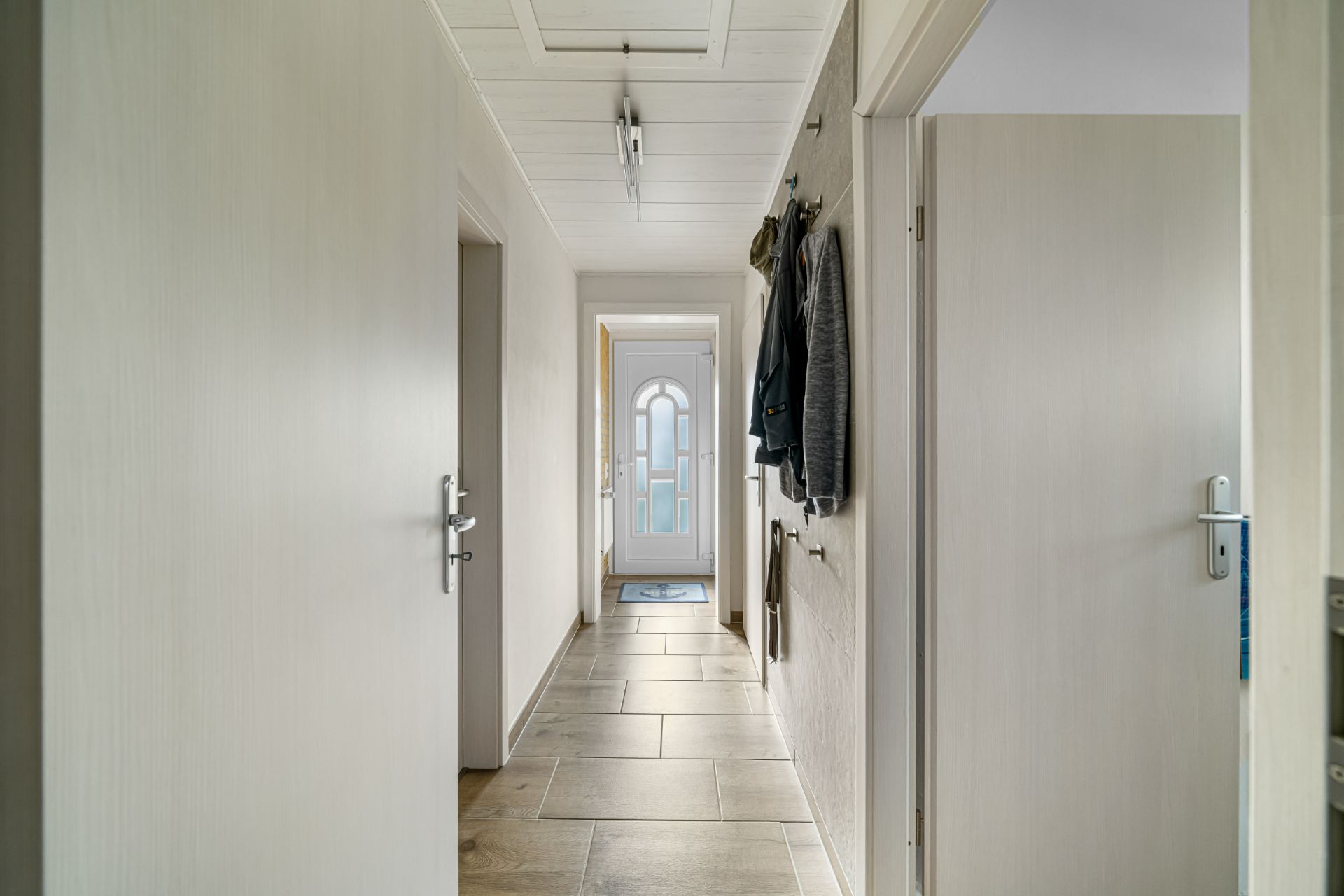Heller Flur mit Fliesenboden, mehreren Türen und Garderobe an der Wand.