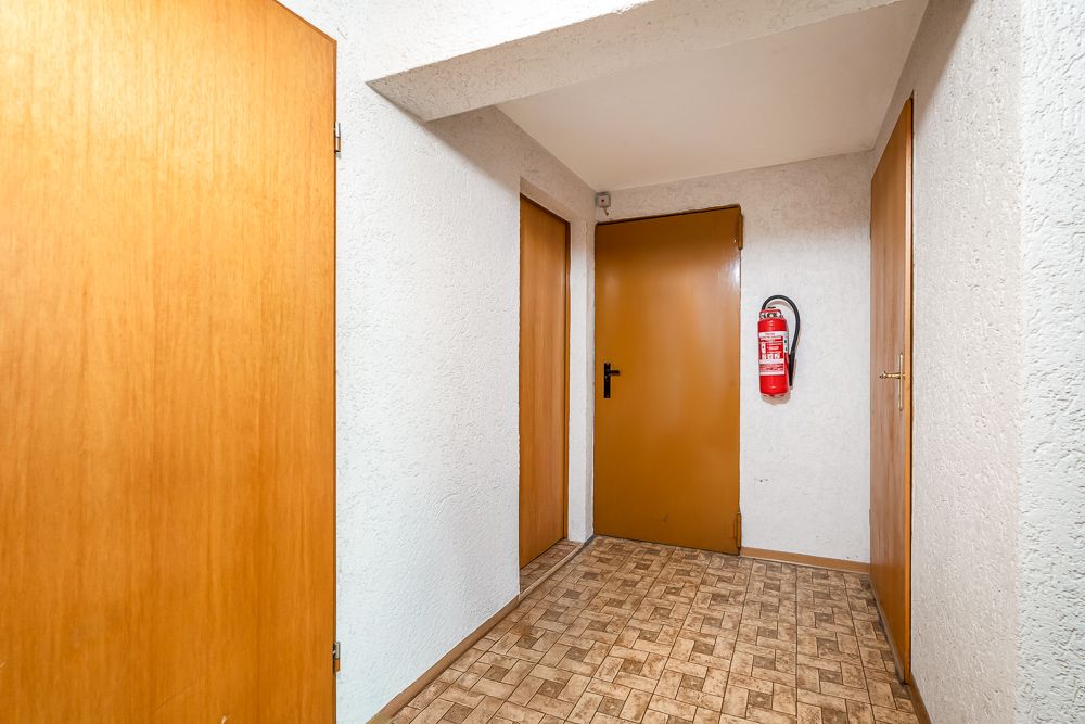 Flur mit vier braunen Türen, weißer Wand und Feuerlöscher an der Wand.