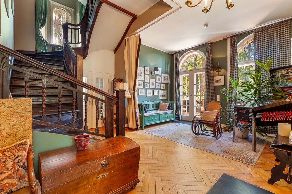 Helles Wohnzimmer mit Holztreppe, Bildern an der Wand, Sitzbank, Schaukelstuhl und Pflanzen.