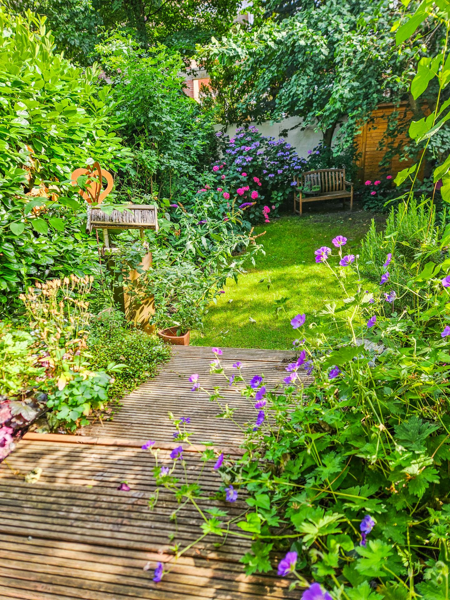 Grüner Garten mit Holzboden, blühenden Blumen und zwei Holzbänken im Hintergrund.