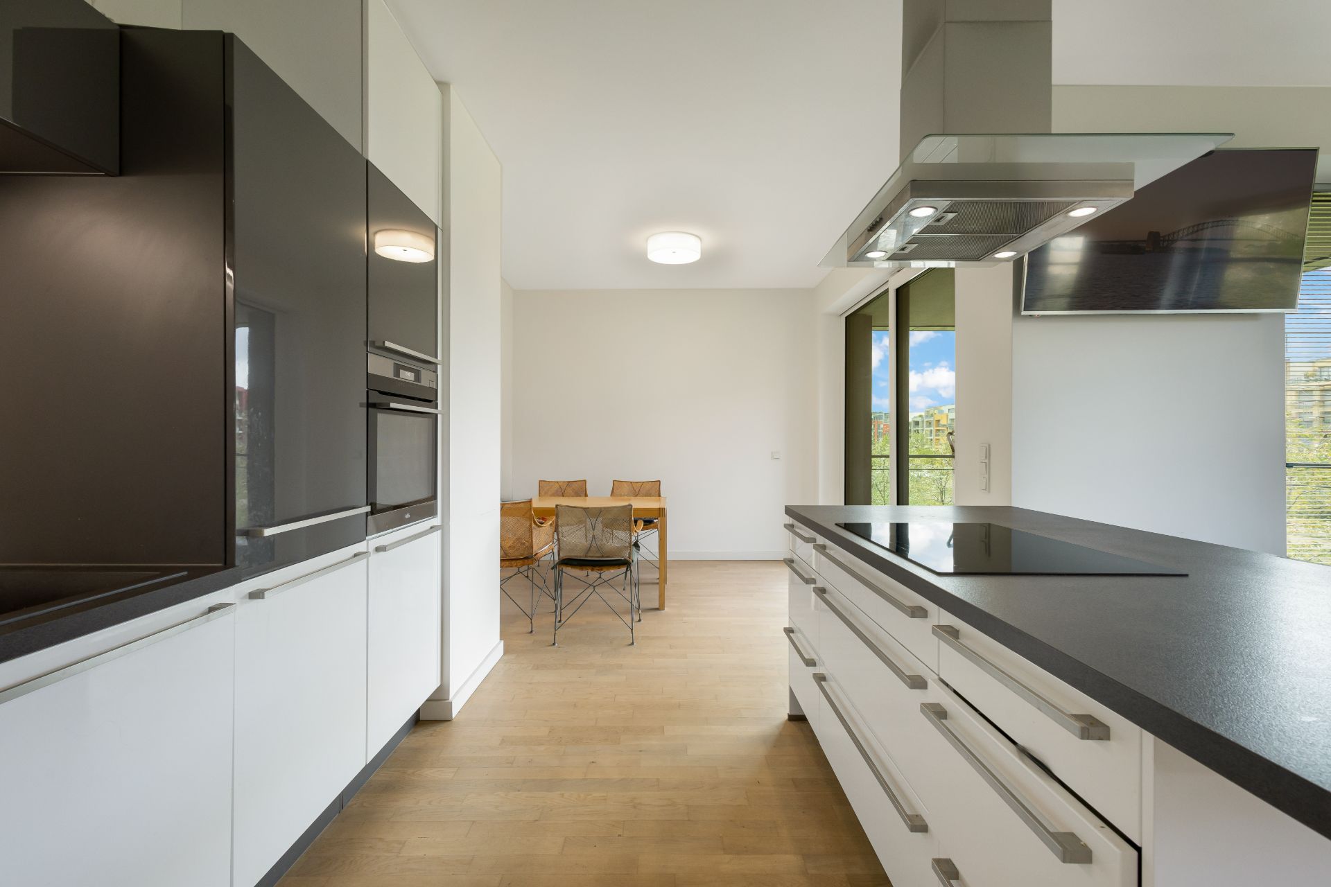 Moderne Küche mit Kochinsel, weißen Schränken und Essbereich mit Holztisch und Stühlen.