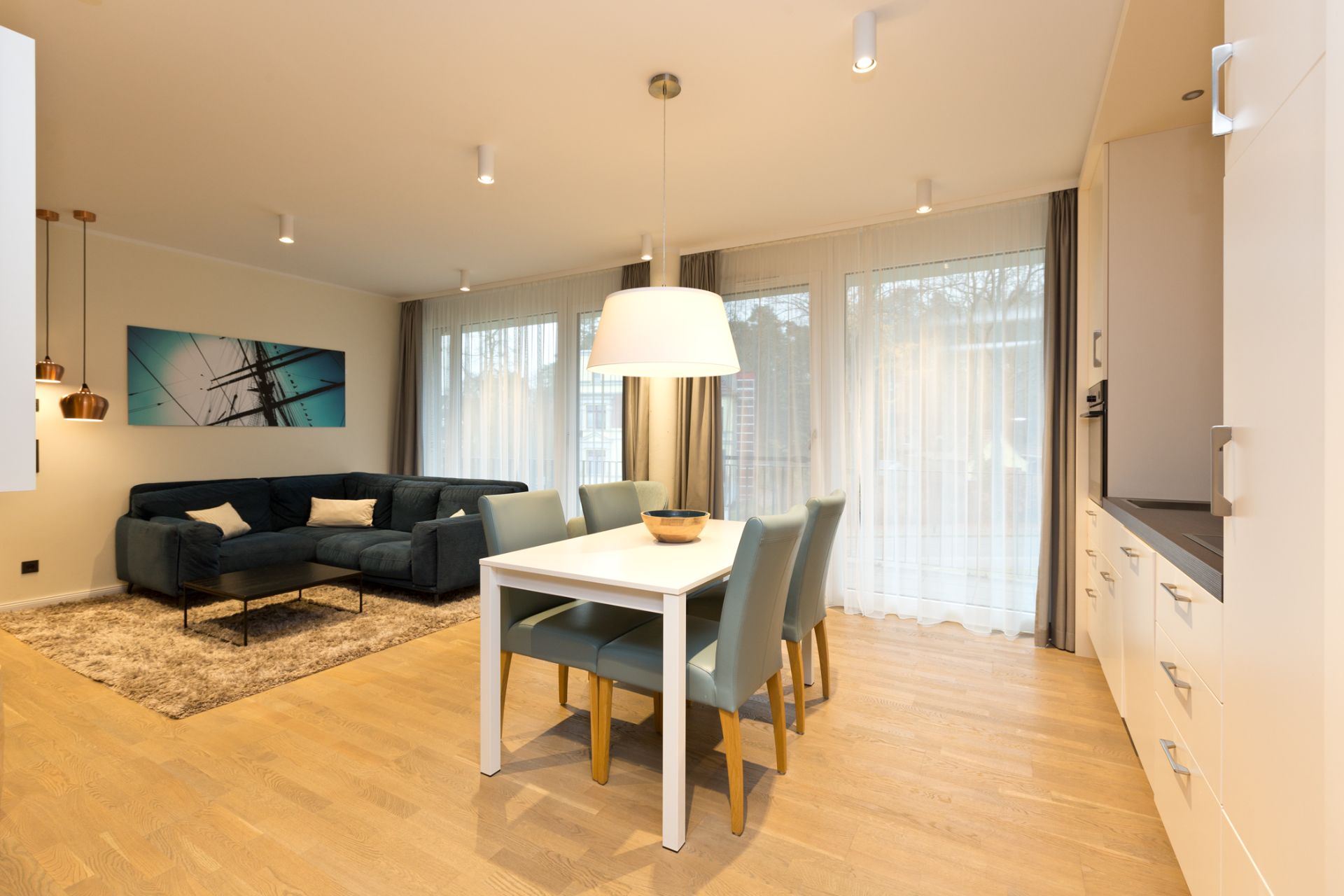 Helles Wohnzimmer mit Ecksofa, Esstisch und vier Stühlen auf Holzfußboden.
