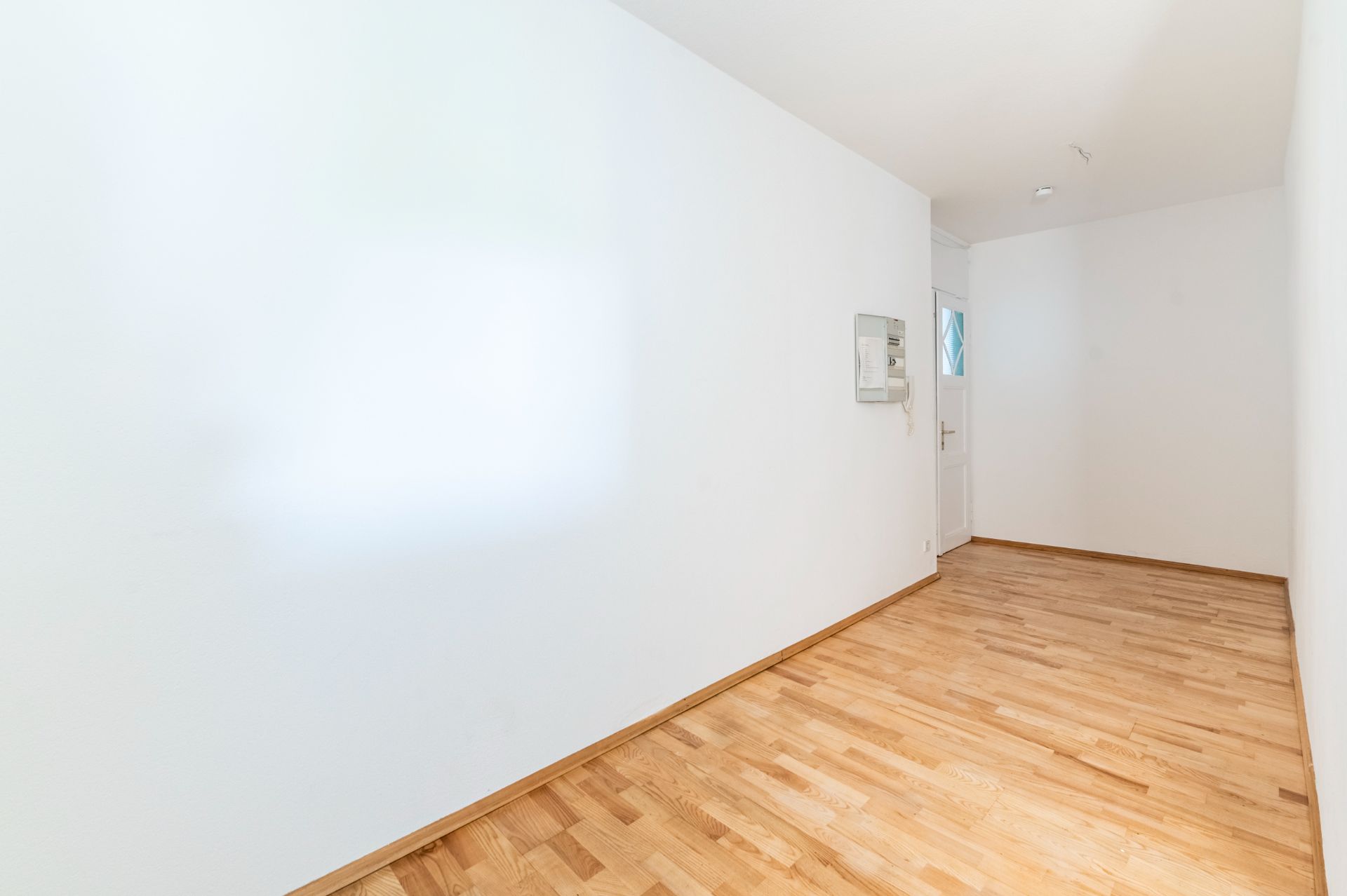 Leerer Flur mit Holzboden, weißen Wänden und Tür am Ende.