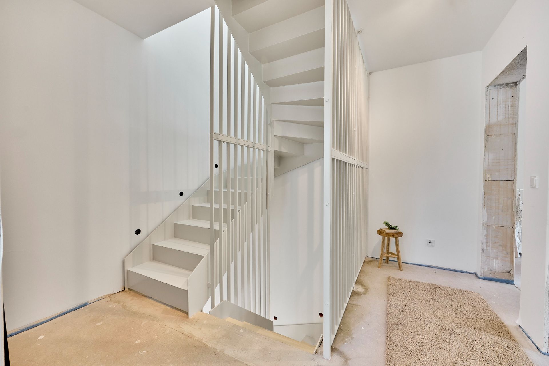 Heller Flur mit weißer, offener Wendeltreppe und Hocker an der Wand.
