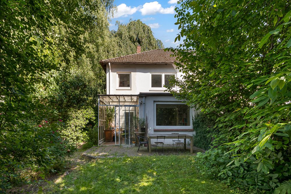 Zweistöckiges Haus mit Terrasse und Garten, umgeben von vielen Bäumen und Grünpflanzen.