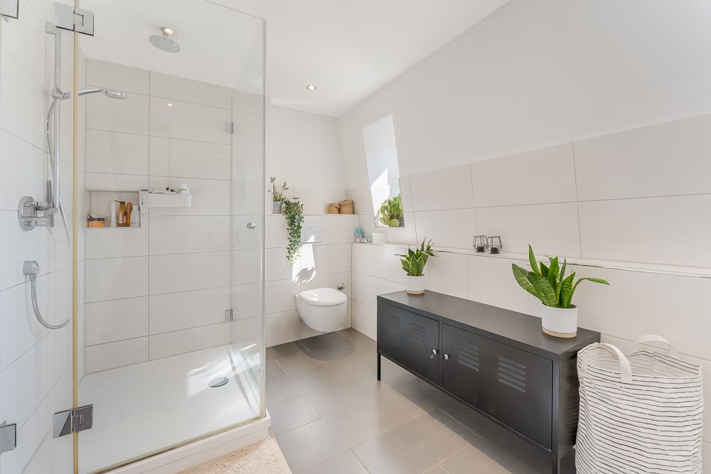 Modernes Badezimmer mit großer Dusche, Hänge-WC, Sideboard, Pflanzen und Wäschekorb.