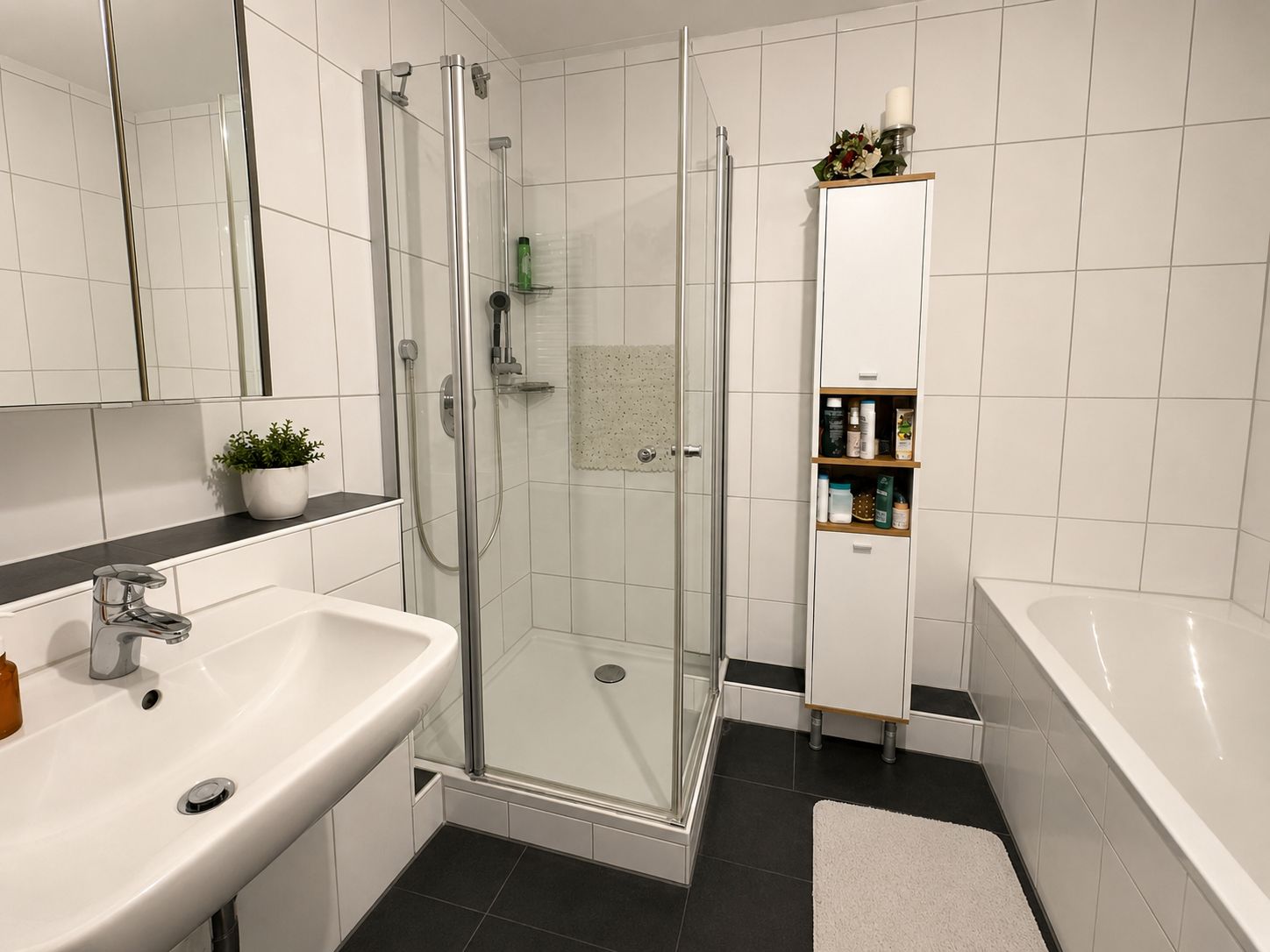 Modernes Badezimmer mit Dusche, Waschbecken, Badewanne und hohem Schrank.