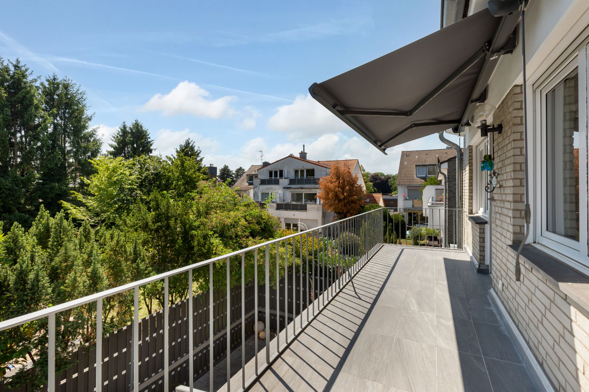 Großer Balkon mit Markise, Blick auf Bäume und benachbarte Häuser.
