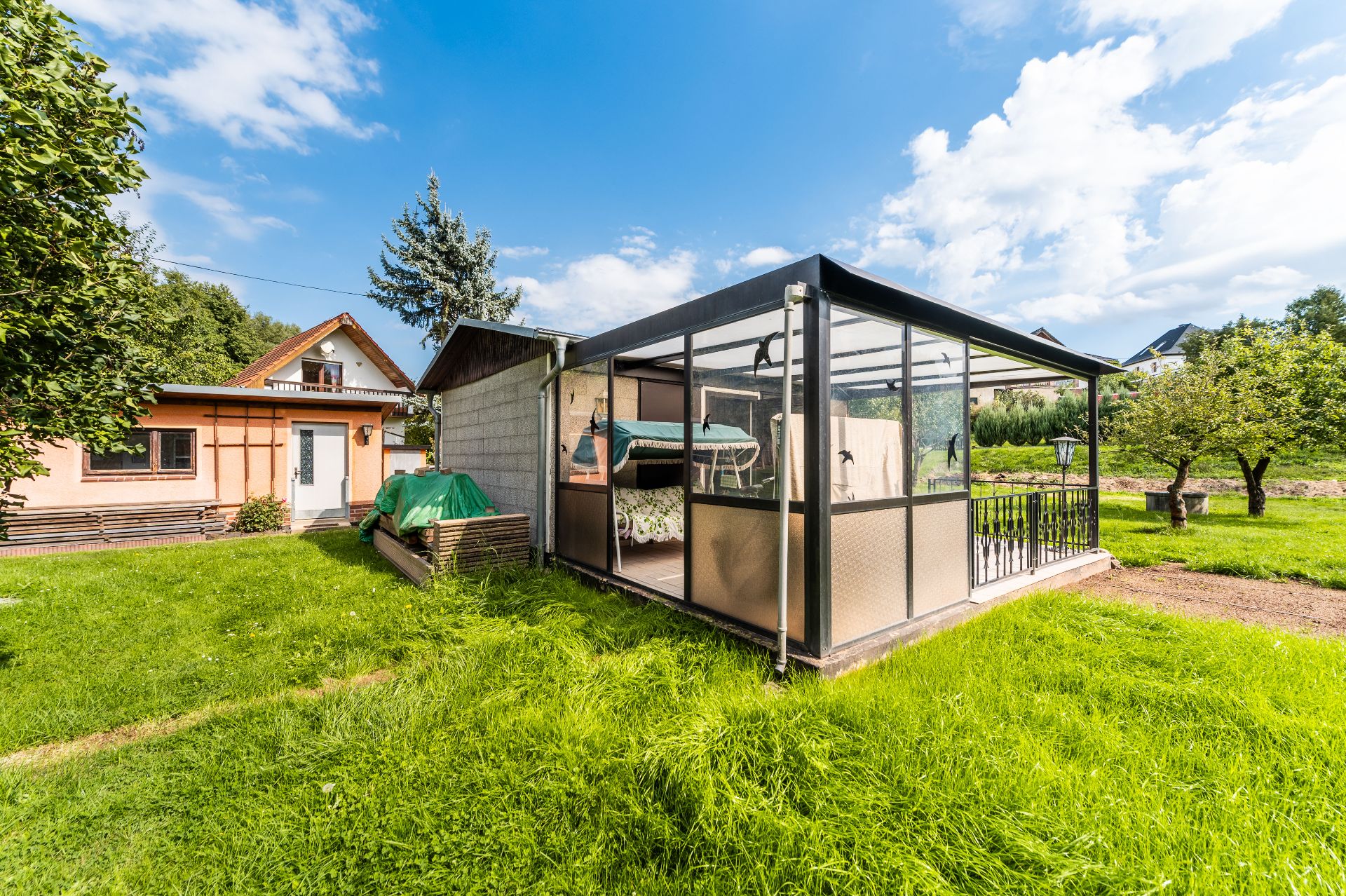 Garten mit verglastem Pavillon, Rasenfläche und einem Haus im Hintergrund.