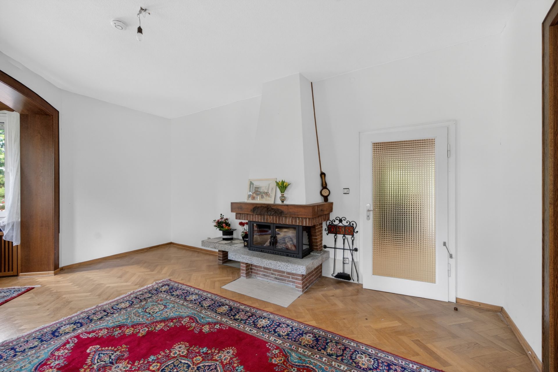 Wohnzimmer mit Teppich, Kamin und Glastür, Holzboden und Dekoration auf dem Kamin.