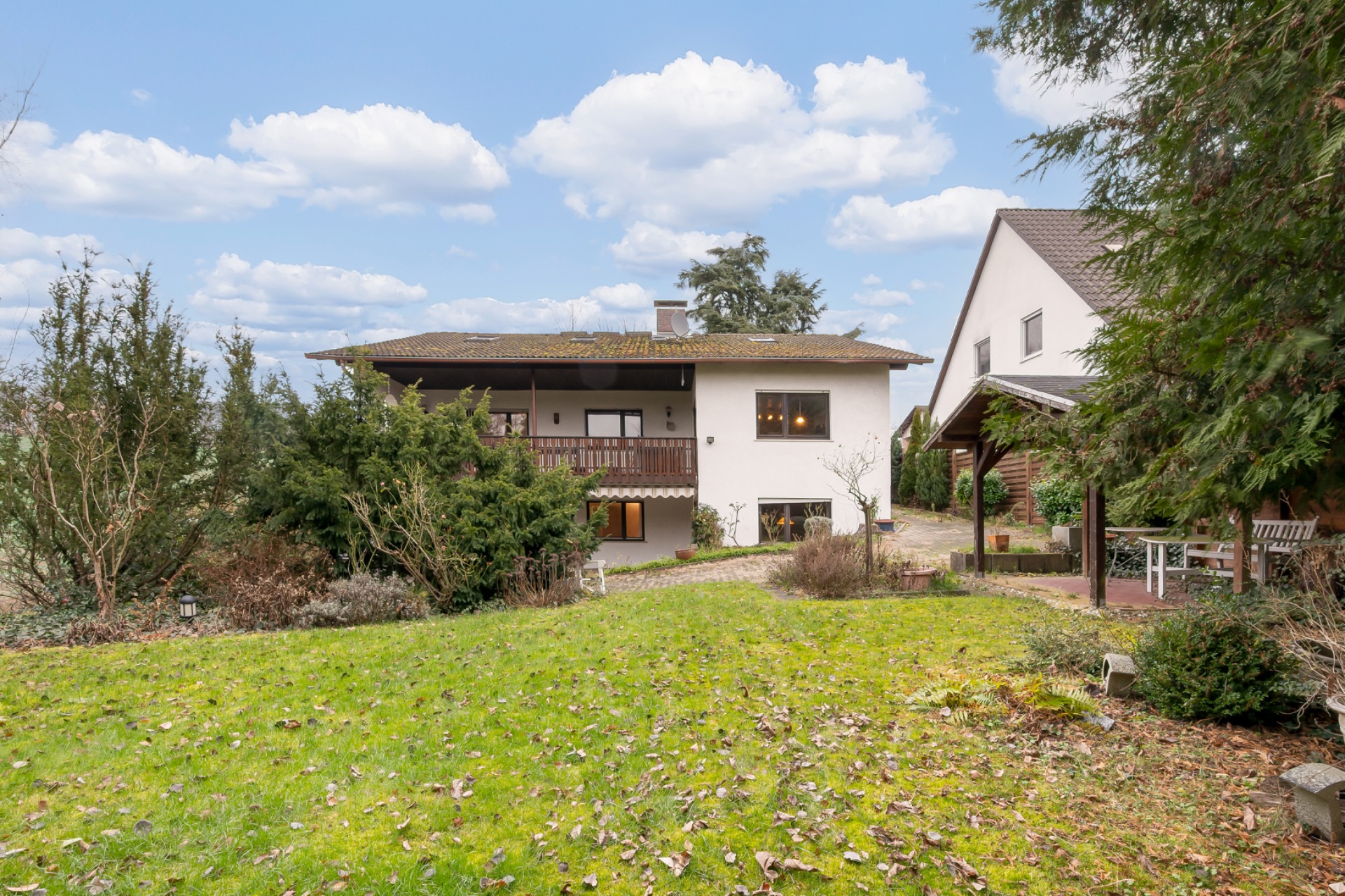 Zweistöckiges Wohnhaus mit Balkon, großem Garten und benachbartem Haus bei Tageslicht.