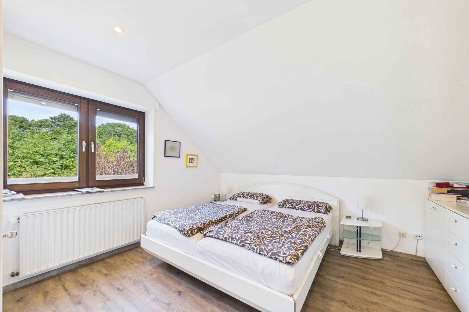Helles Schlafzimmer mit Doppelbett, Holzboden, Dachschräge und großem Fenster mit Blick ins Grüne.