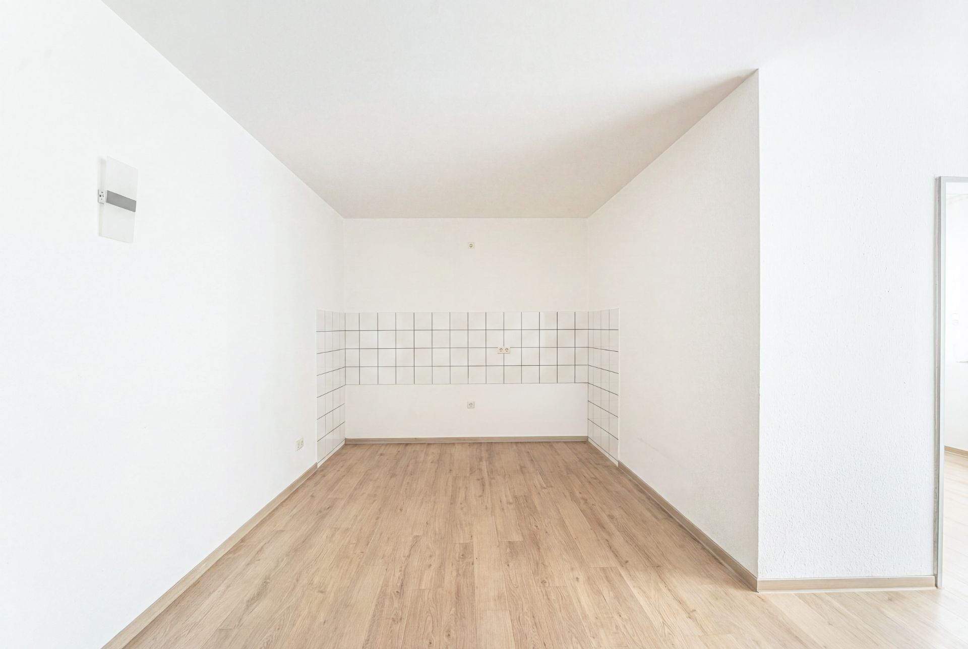 Leerer Raum mit weiß gekachelter Ecke und hellem Holzboden.