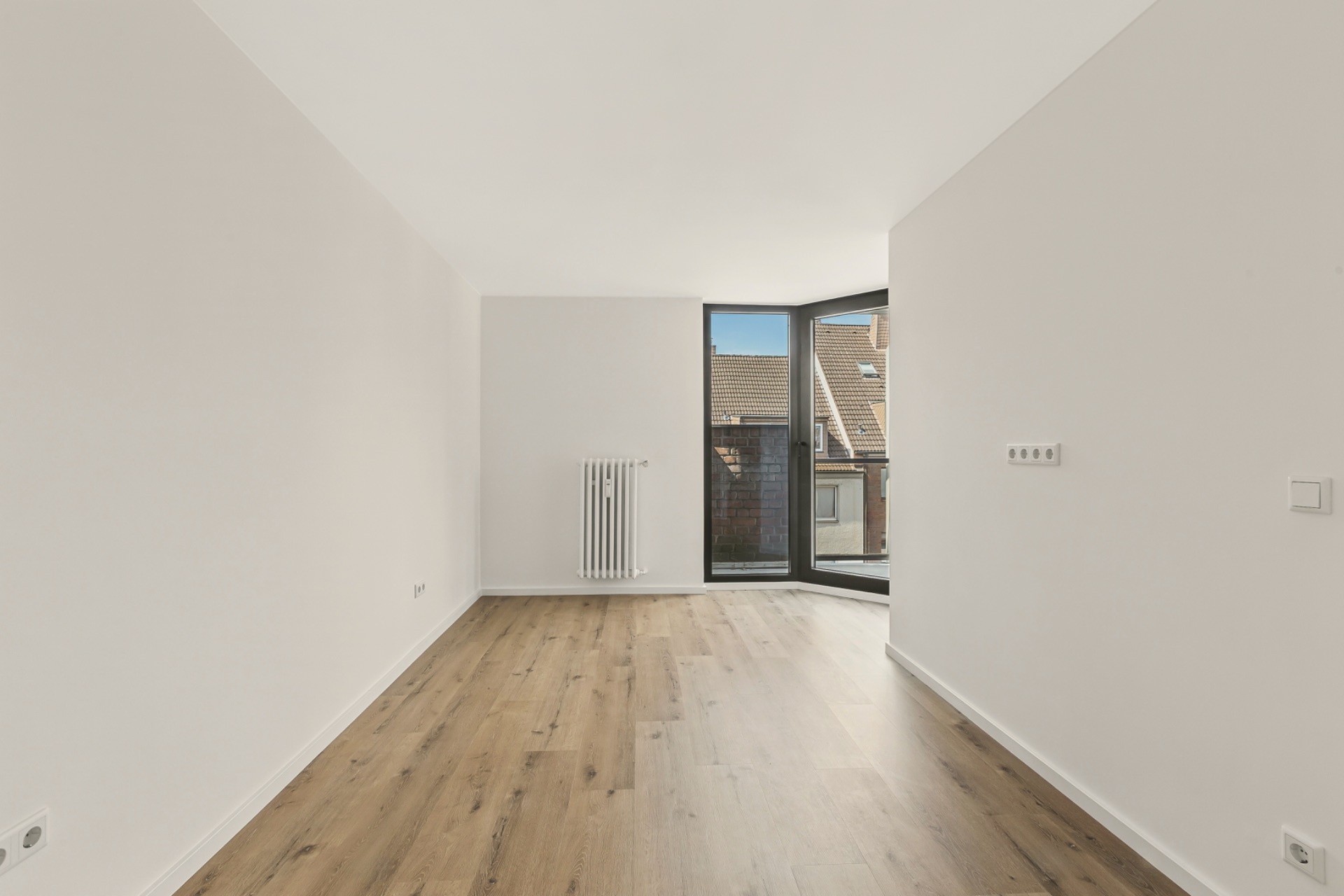 Leerer Raum mit Holzfußboden, weißer Wand, Fenster und Heizkörper.