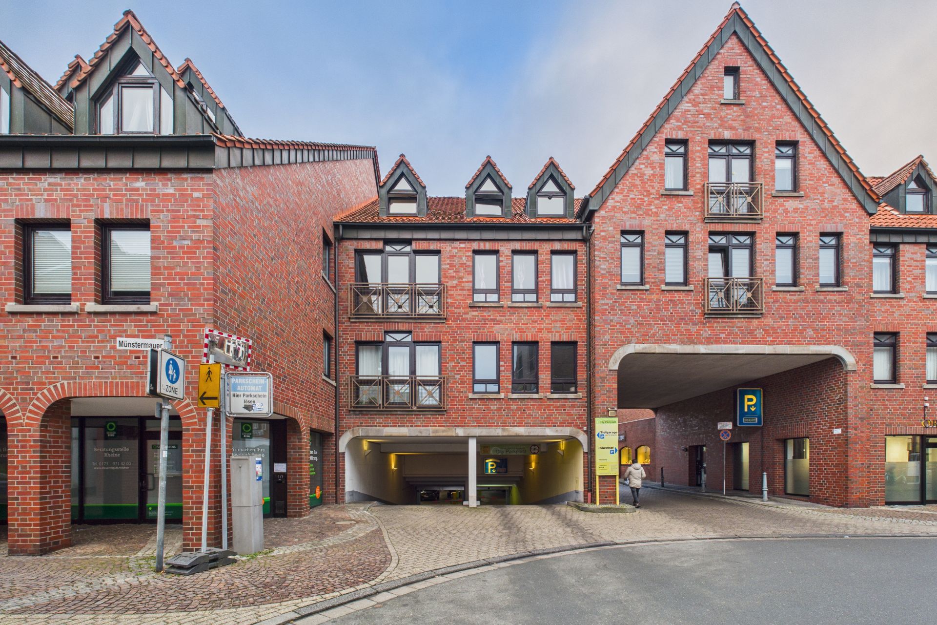 Rotes Backsteingebäude mit mehreren Fenstern und zwei Einfahrten zu einer Tiefgarage.