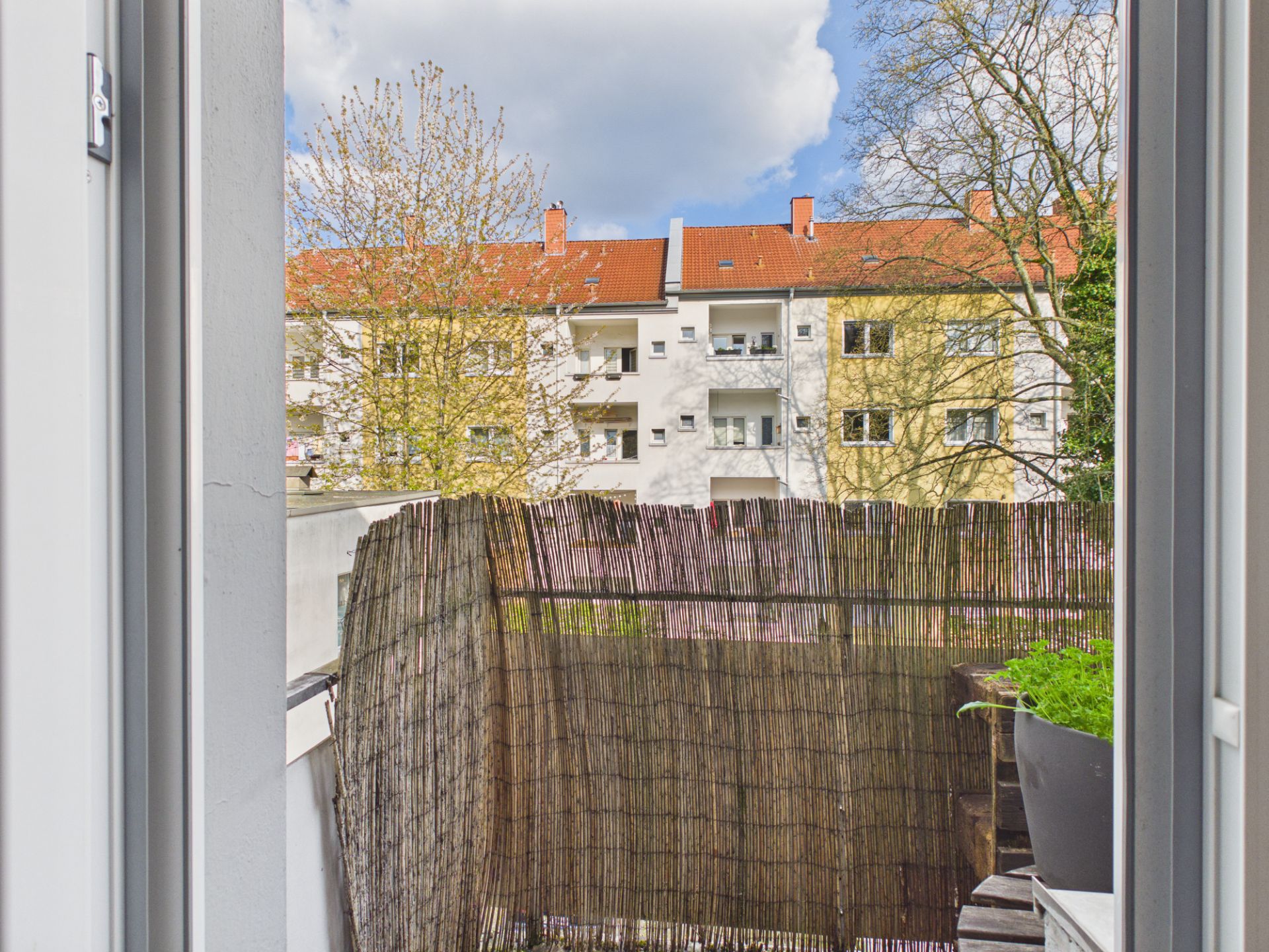 Blick von einer Wohnung auf einen kleinen Balkon mit Sichtschutz und Nachbarhäuser.
