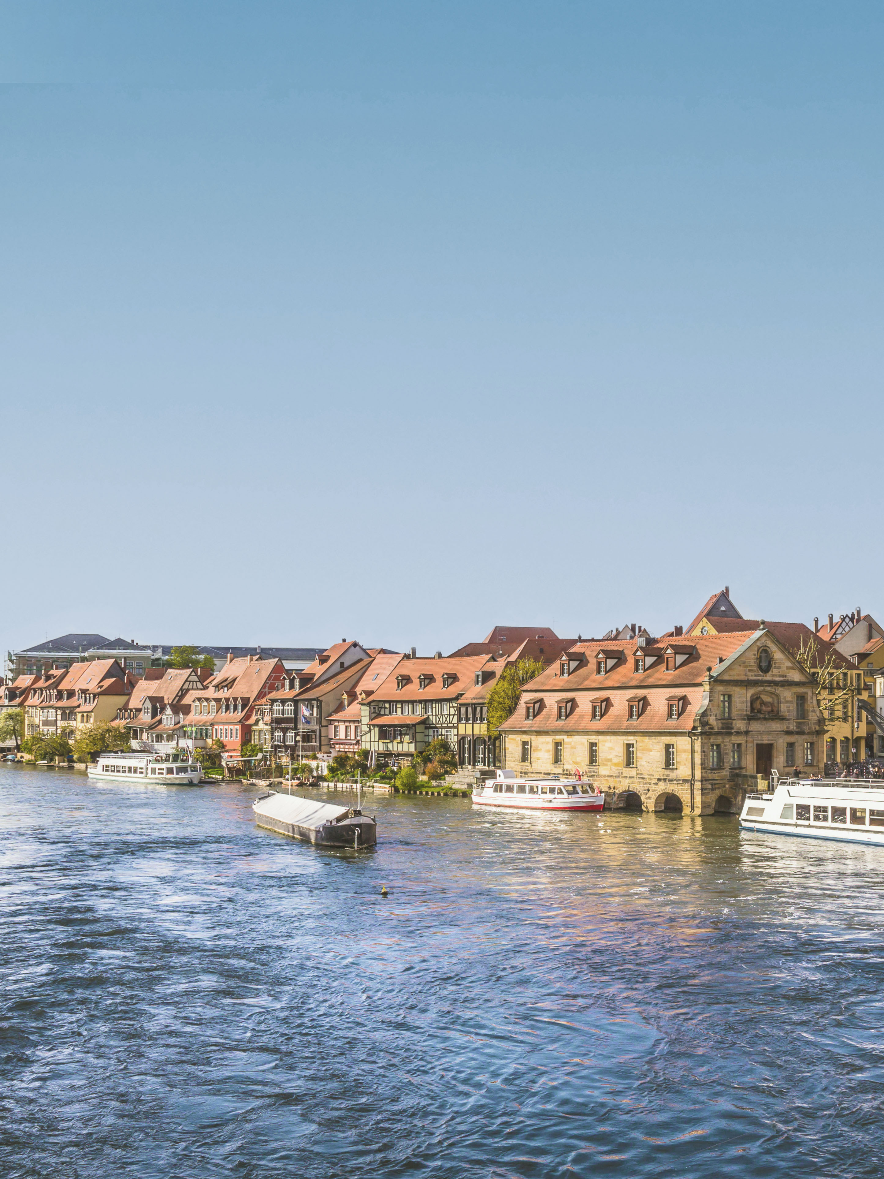 Reihe von Wohnhäusern mit roten Dächern am Flussufer, Boote auf dem Wasser.