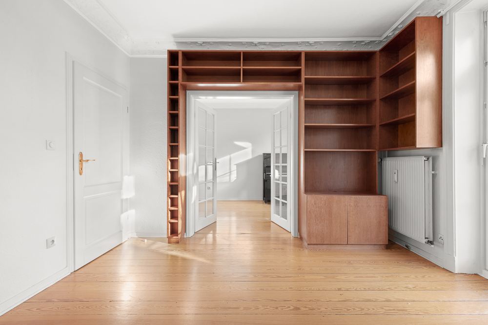 Helles Zimmer mit Holzboden, eingebautem Regal und weißen Doppeltüren.