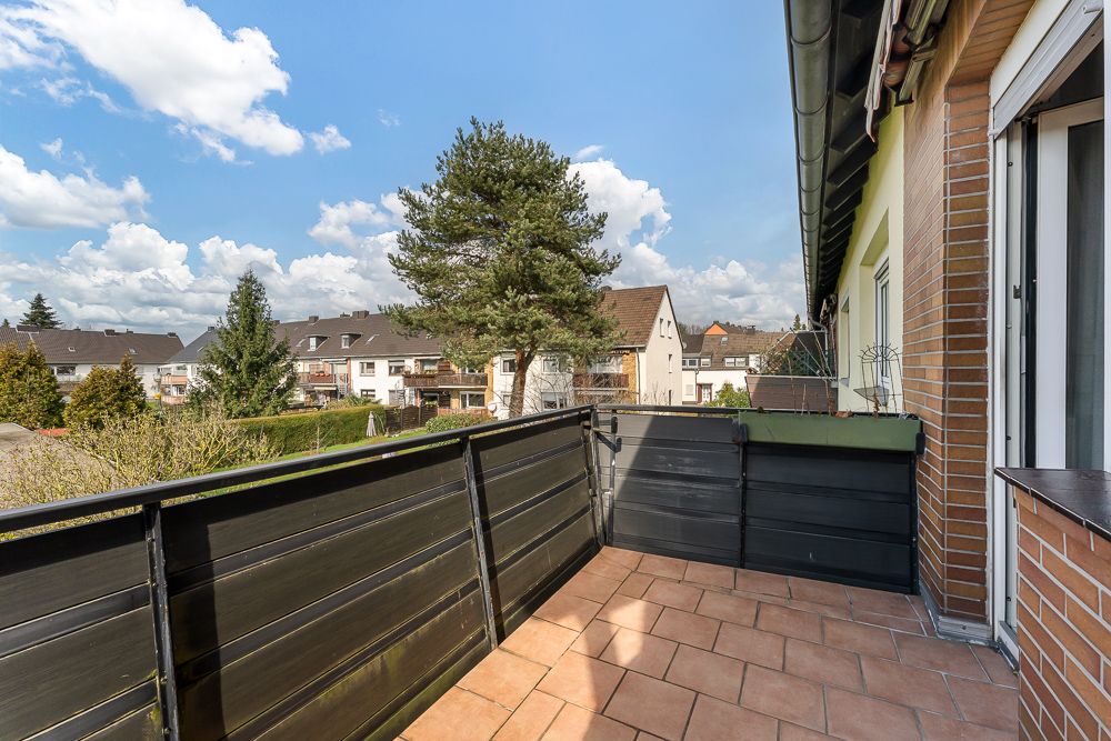 Balkon mit braunen Fliesen und schwarzem Geländer, Blick auf Wohnhäuser und Bäume.