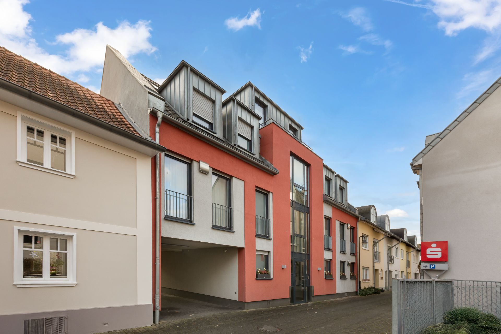 Mehrfamilienhaus mit roter Fassade, mehreren Fenstern und einem Durchgang im Erdgeschoss.