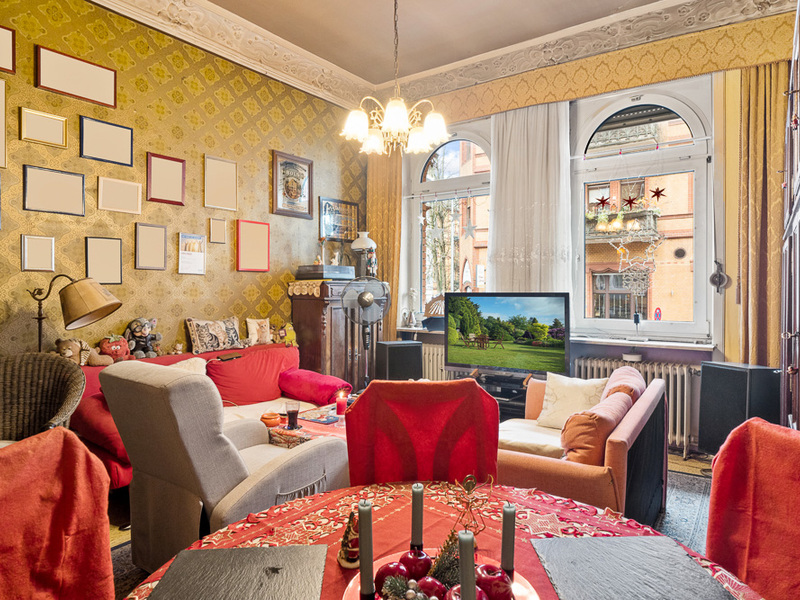 Gemütliches Wohnzimmer mit Sofas, TV, vielen Bildern an der Wand und großen Fenstern.