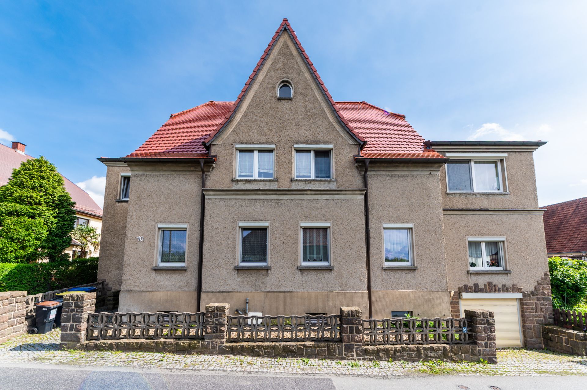 Vorderansicht eines zweistöckigen Wohnhauses mit rotem Dach und kleinem Vorgarten.