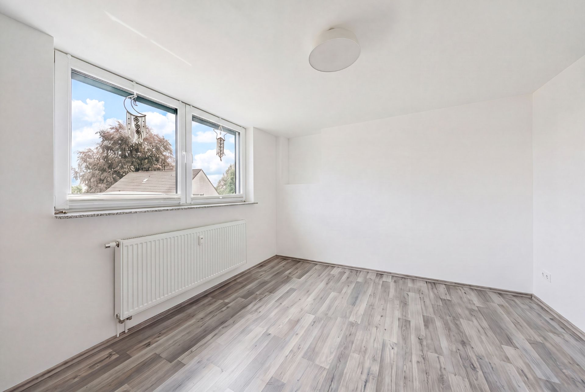 Heller, leerer Raum mit Holzfußboden, weißen Wänden und drei Fenstern.