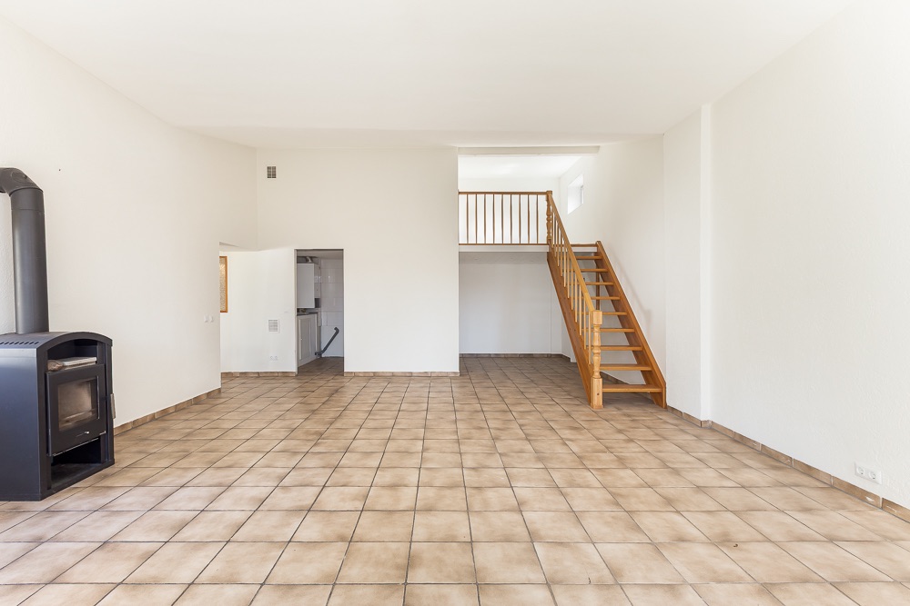 Heller Raum mit Kaminofen, Fliesenboden und Holztreppe zu einer offenen Galerie.