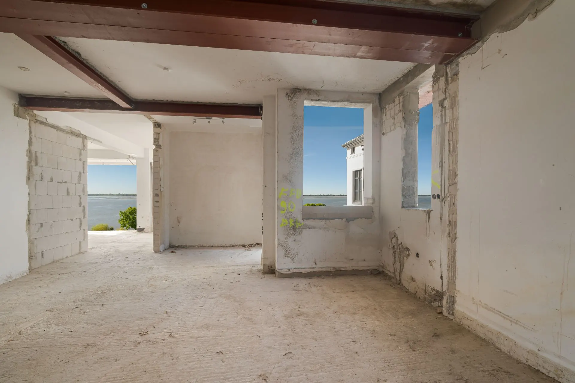Leerer Raum mit unfertigen Wänden und Blick durch Fenster auf das Wasser.