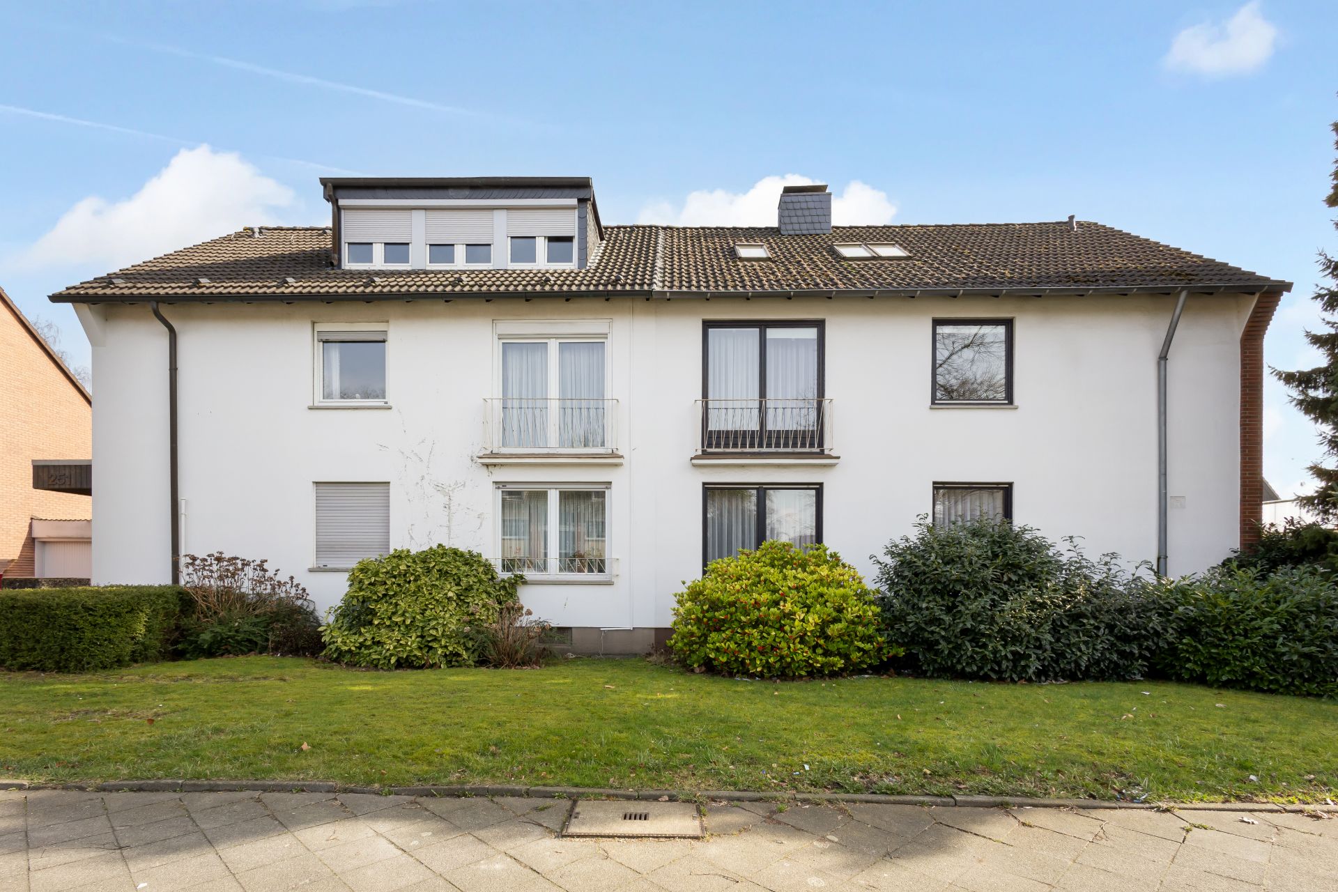 Vorderansicht eines zweistöckigen Wohnhauses mit weißer Fassade und Garten.